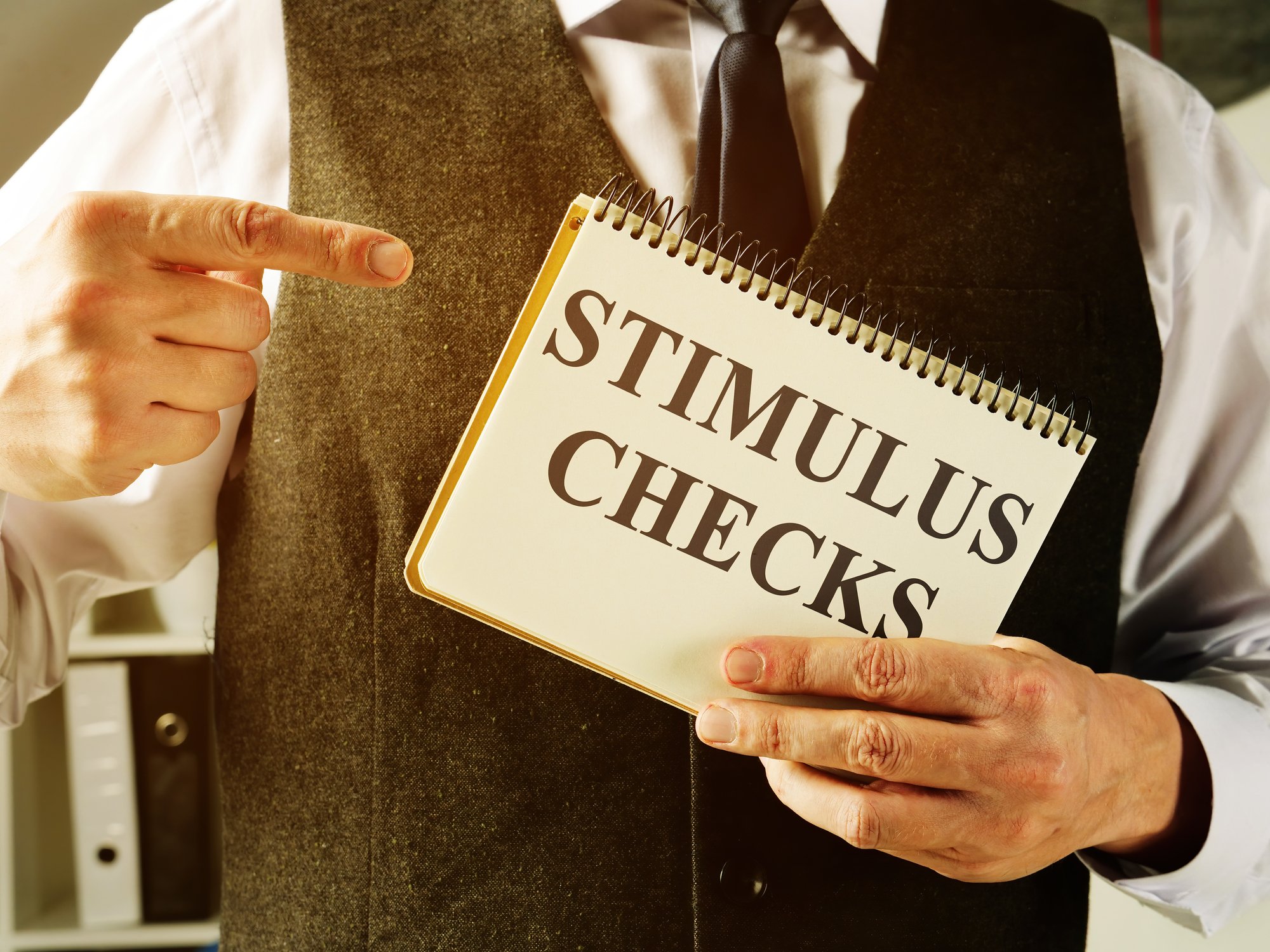 A man holding up a notebook that reads "stimulus checks."