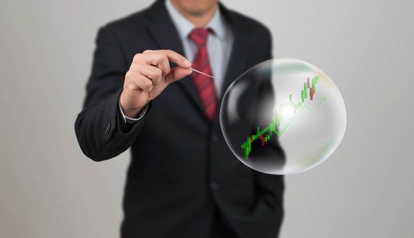 A man in a suit about to pop a bubble with a rising stock chart in it.