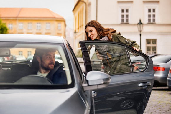 A woman opening a door to get into the back seat of a car. 