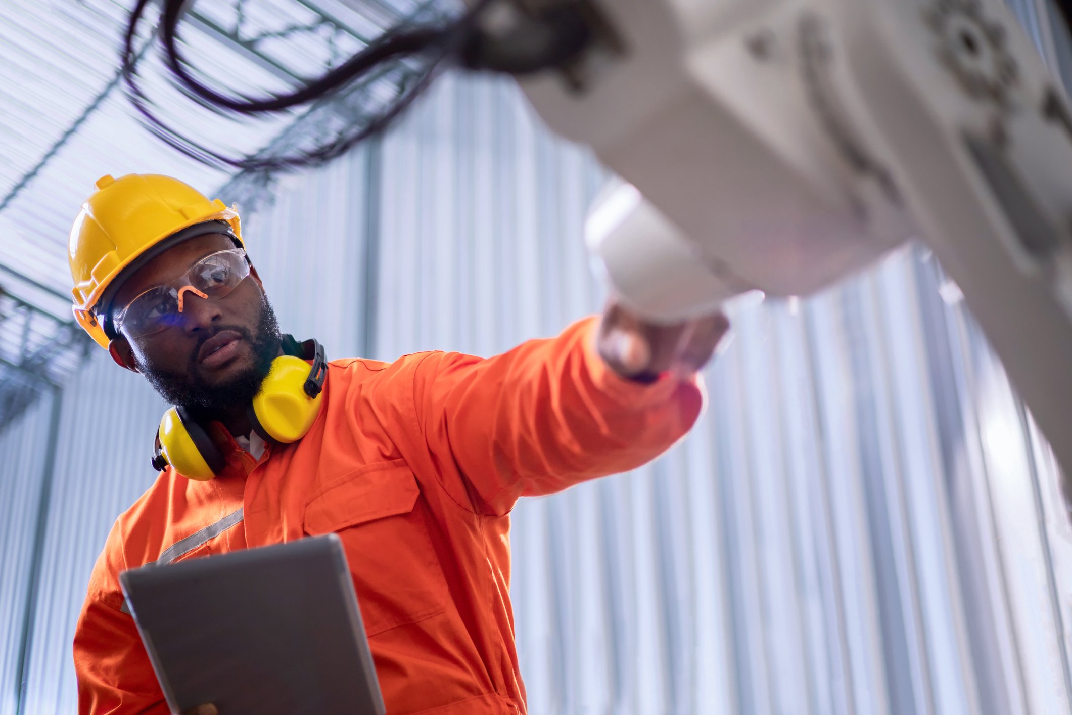 An engineer inspects a robotic arm while working on his tablet. 