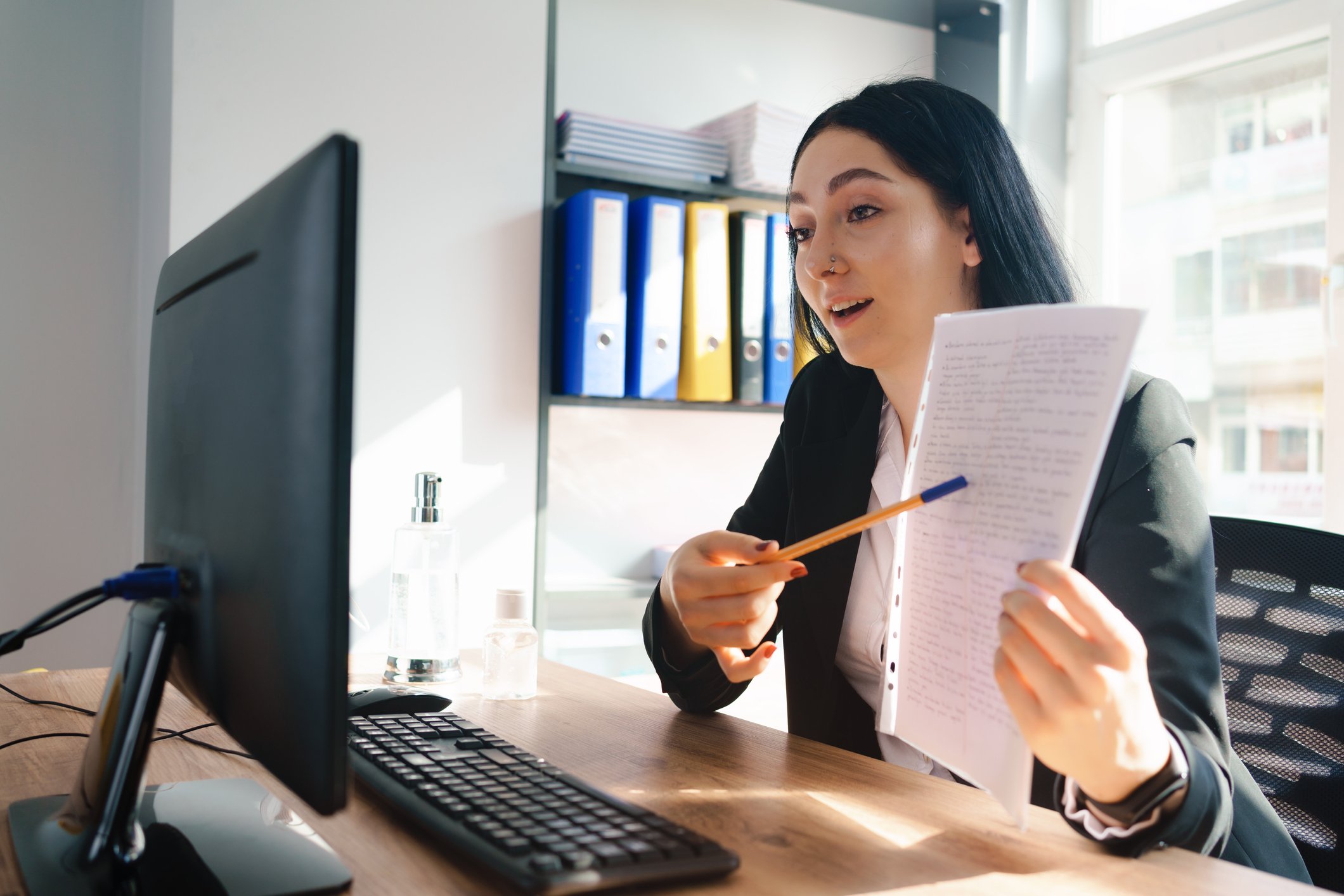 A business person on a Zoom call, making a presentation using data as they point to a document with a pencil. 