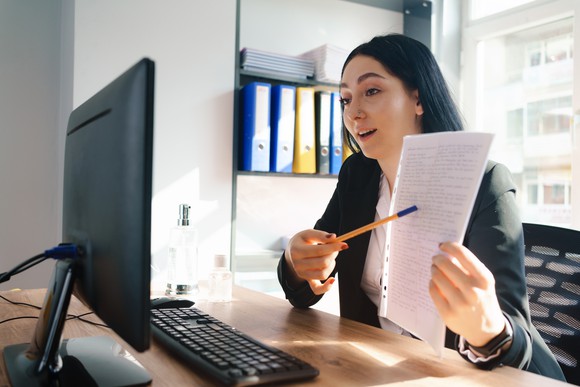 A business person on a Zoom call, making a presentation using data as they point to a document with a pencil. 