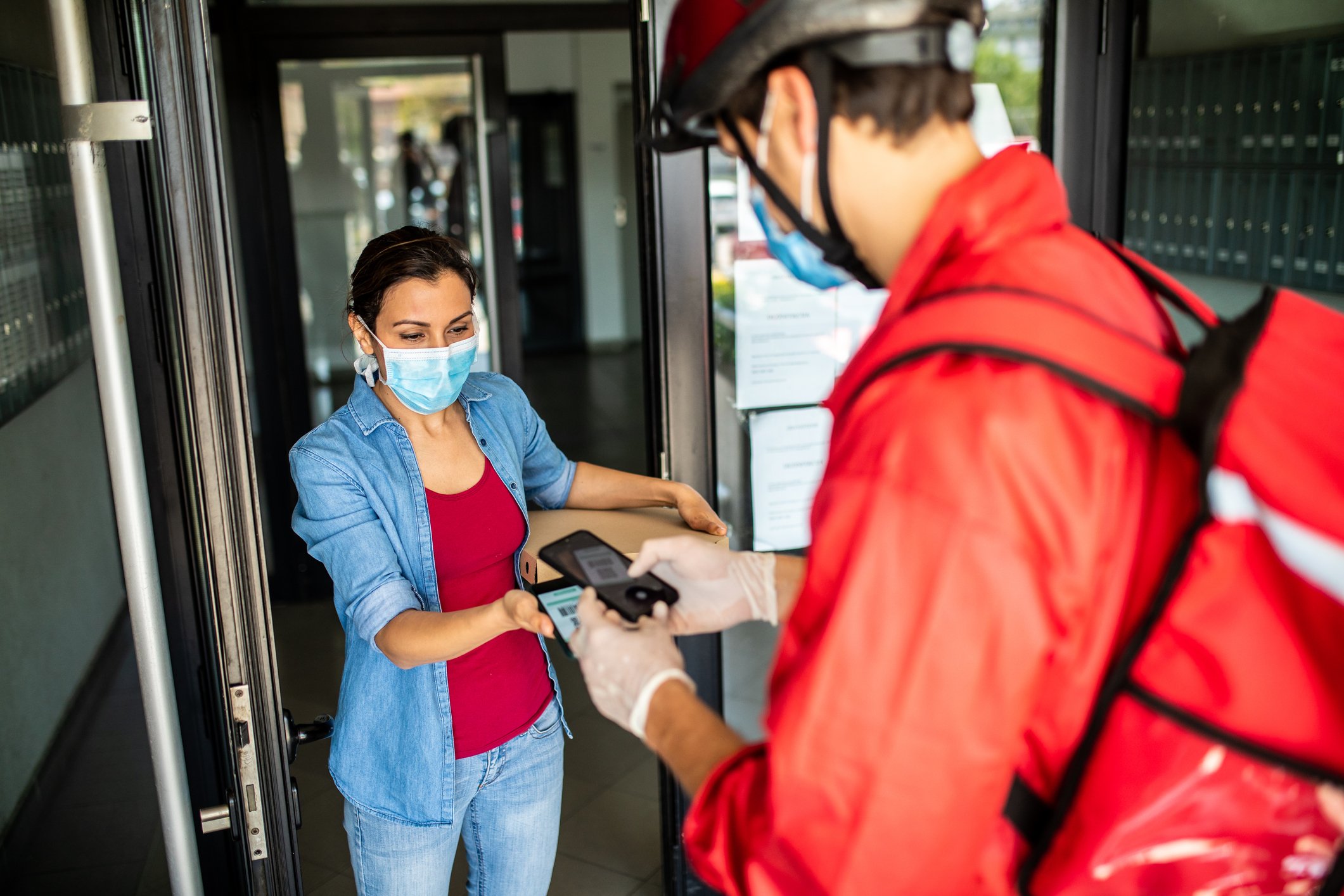 A restaurant delivery driver handing food to a customer standing in a doorway.