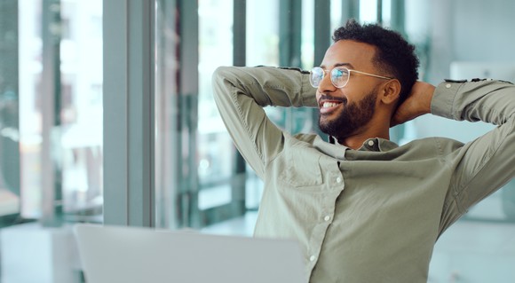 A smiling young man relaxes at his desk.