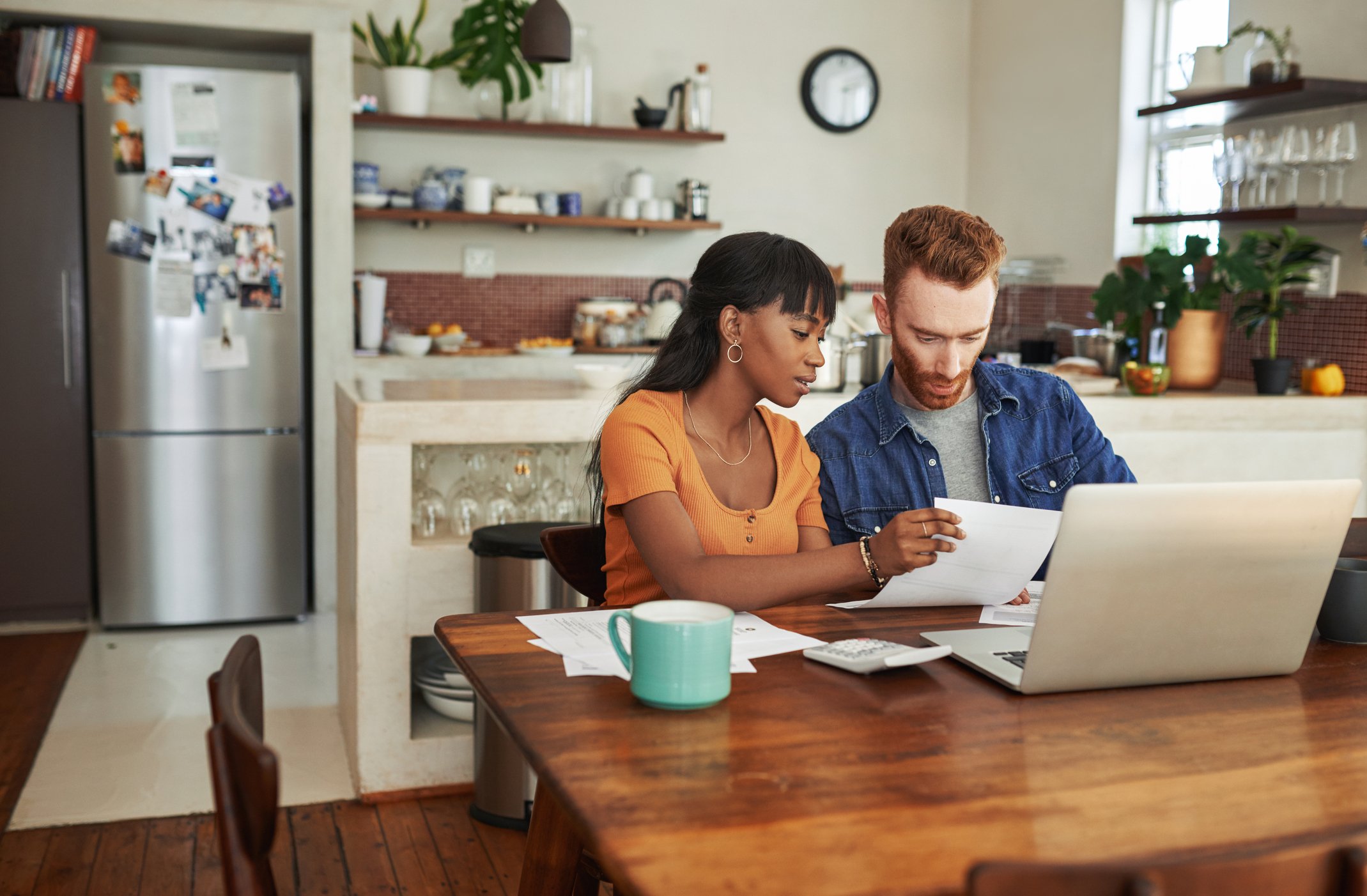 Two people sitting at a kitchen table in front of a computer with a calculator.