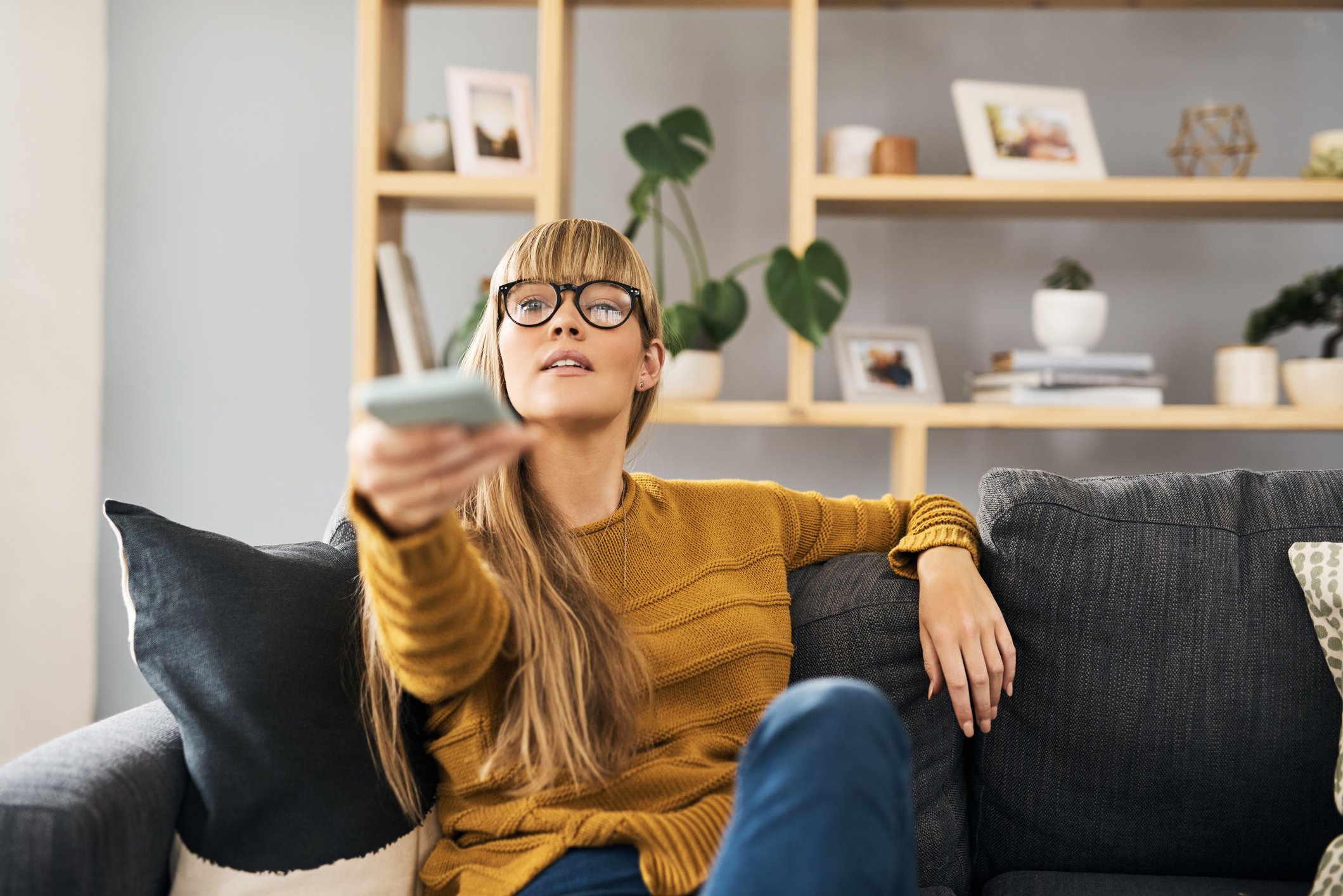 A woman sitting on a couch and pointing a TV remote.