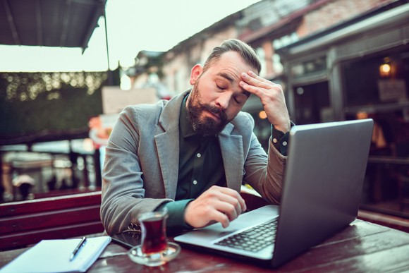 A stressed investor drinks tea at a cafe while working with a laptop computer.