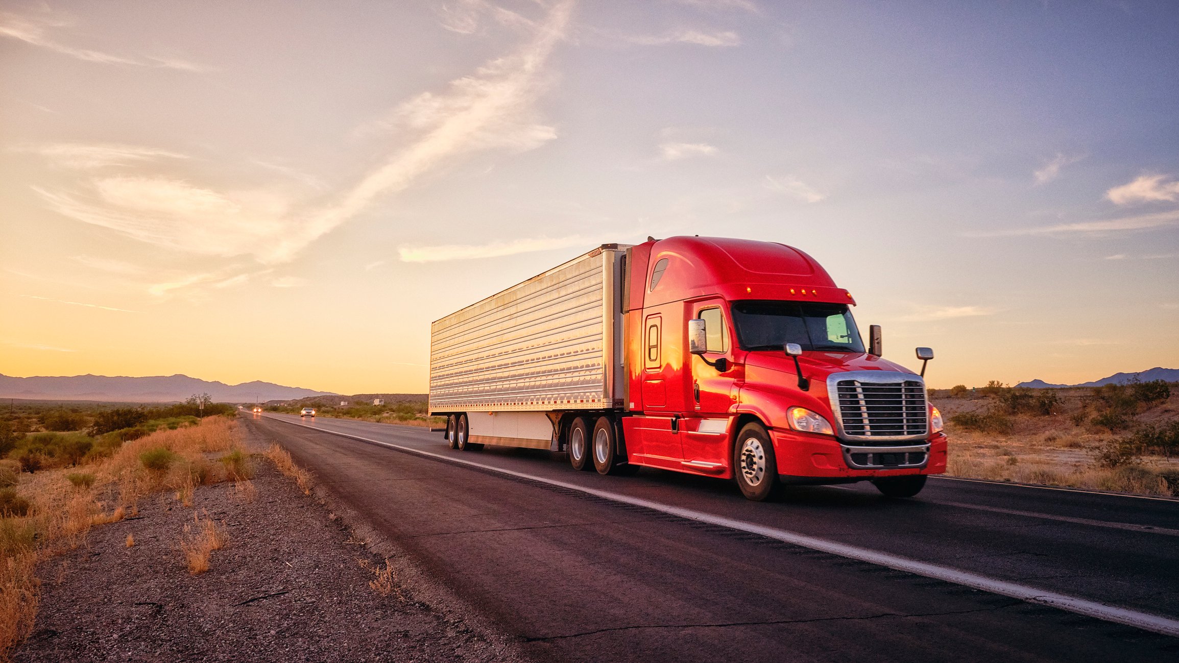 A heavy duty truck hauls cargo down a desert highway. 