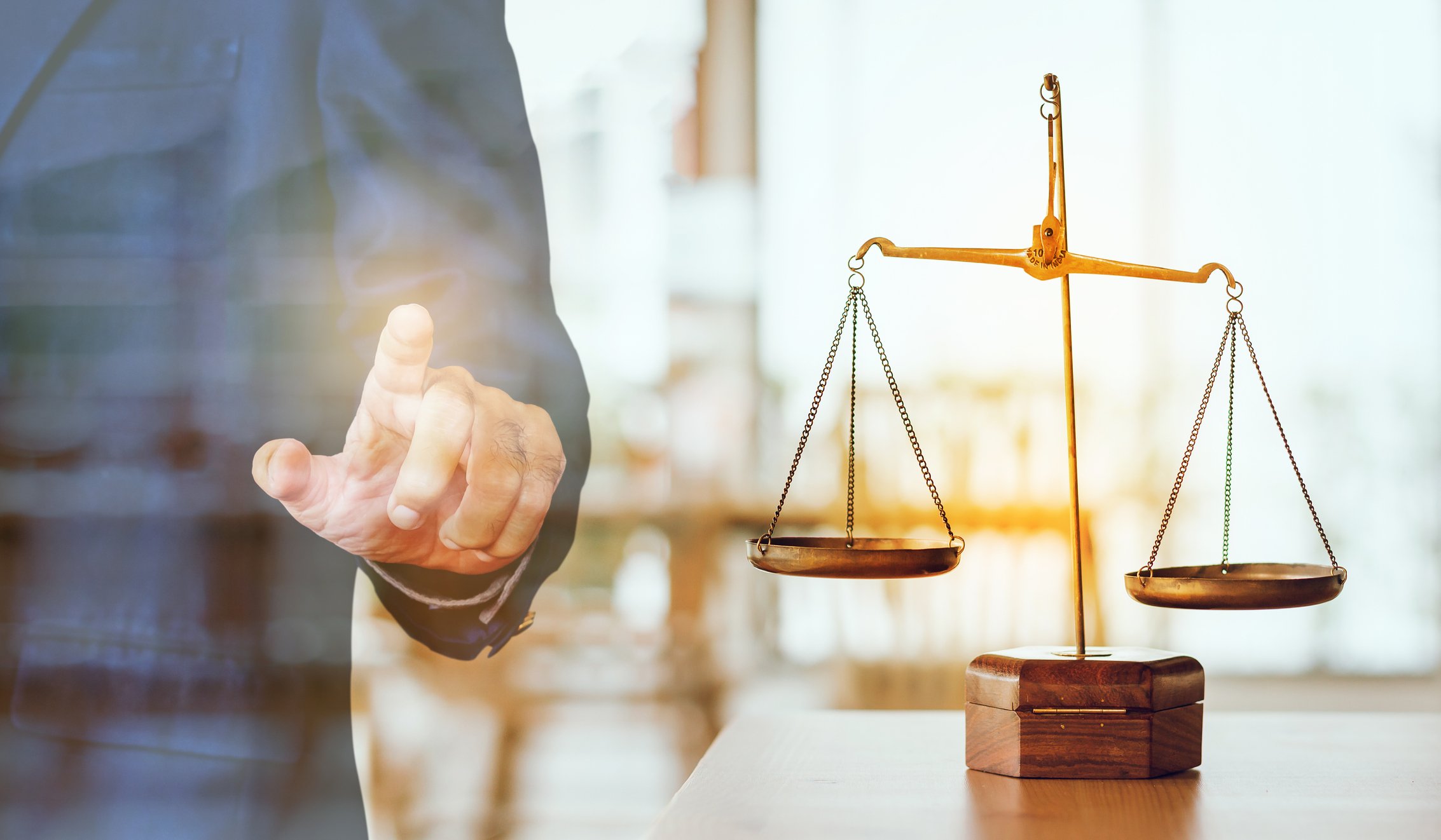 An antique scale sits on a table next to a person's finger.