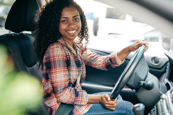 Smiling person sitting in the driver's seat of a car.