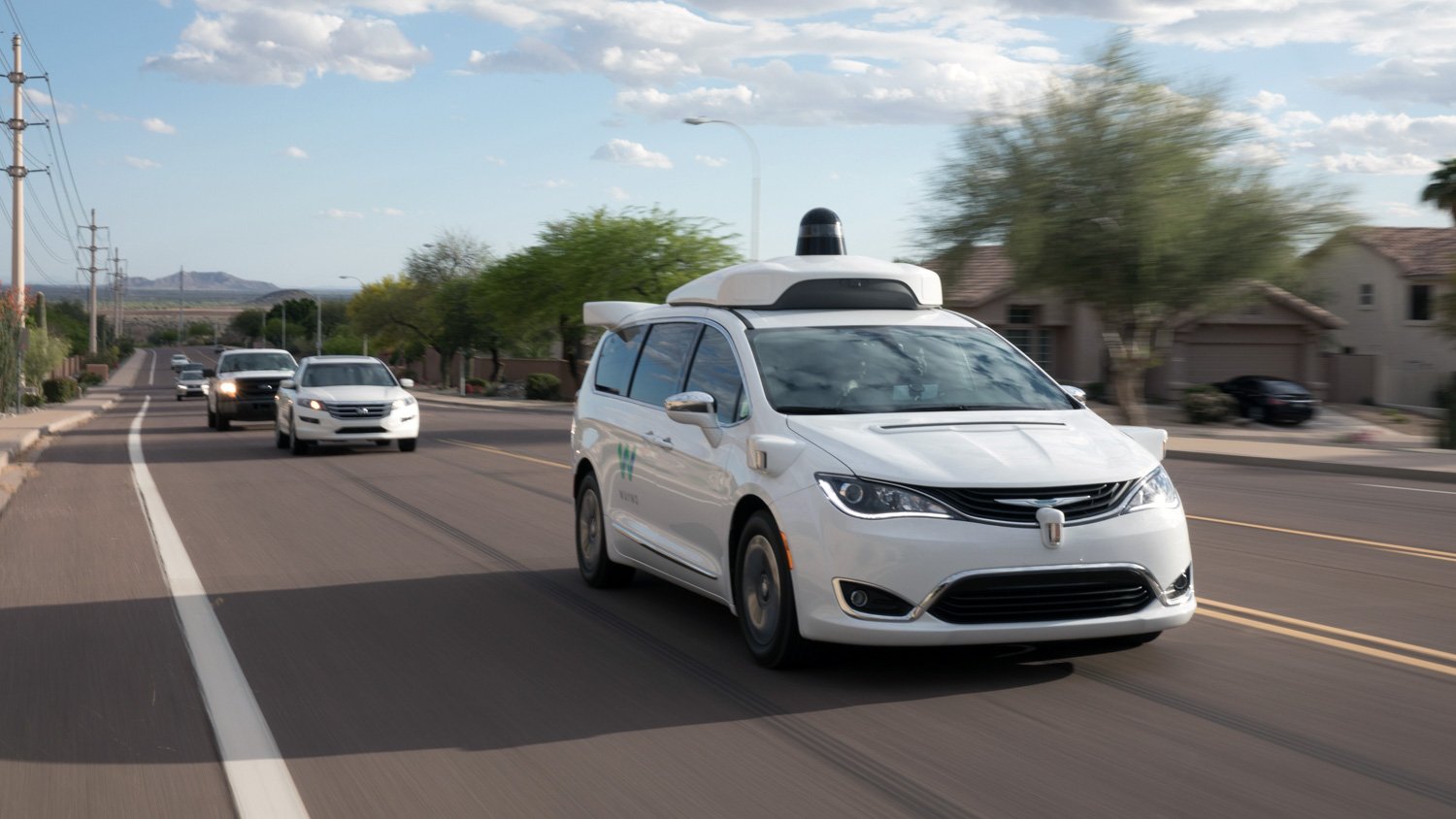 A Wamo vehicle with lidar sensor on top goes down a road with traffic behind it. 