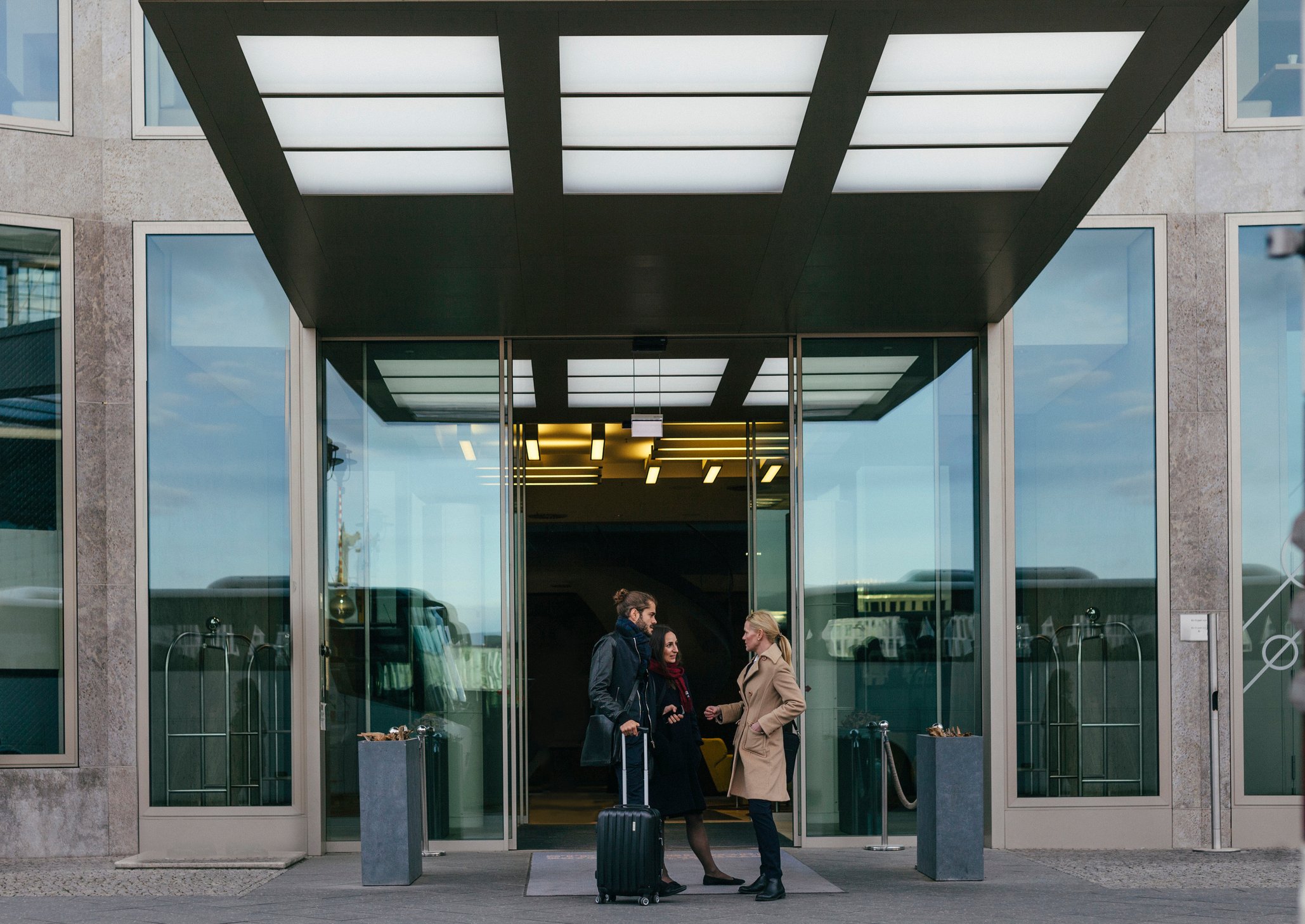 Two people with luggage outside the entrance of hotel.
