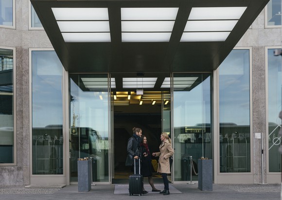 Two people with luggage outside the entrance of hotel.
