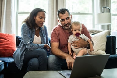 Two people looking at laptop while one holds baby
