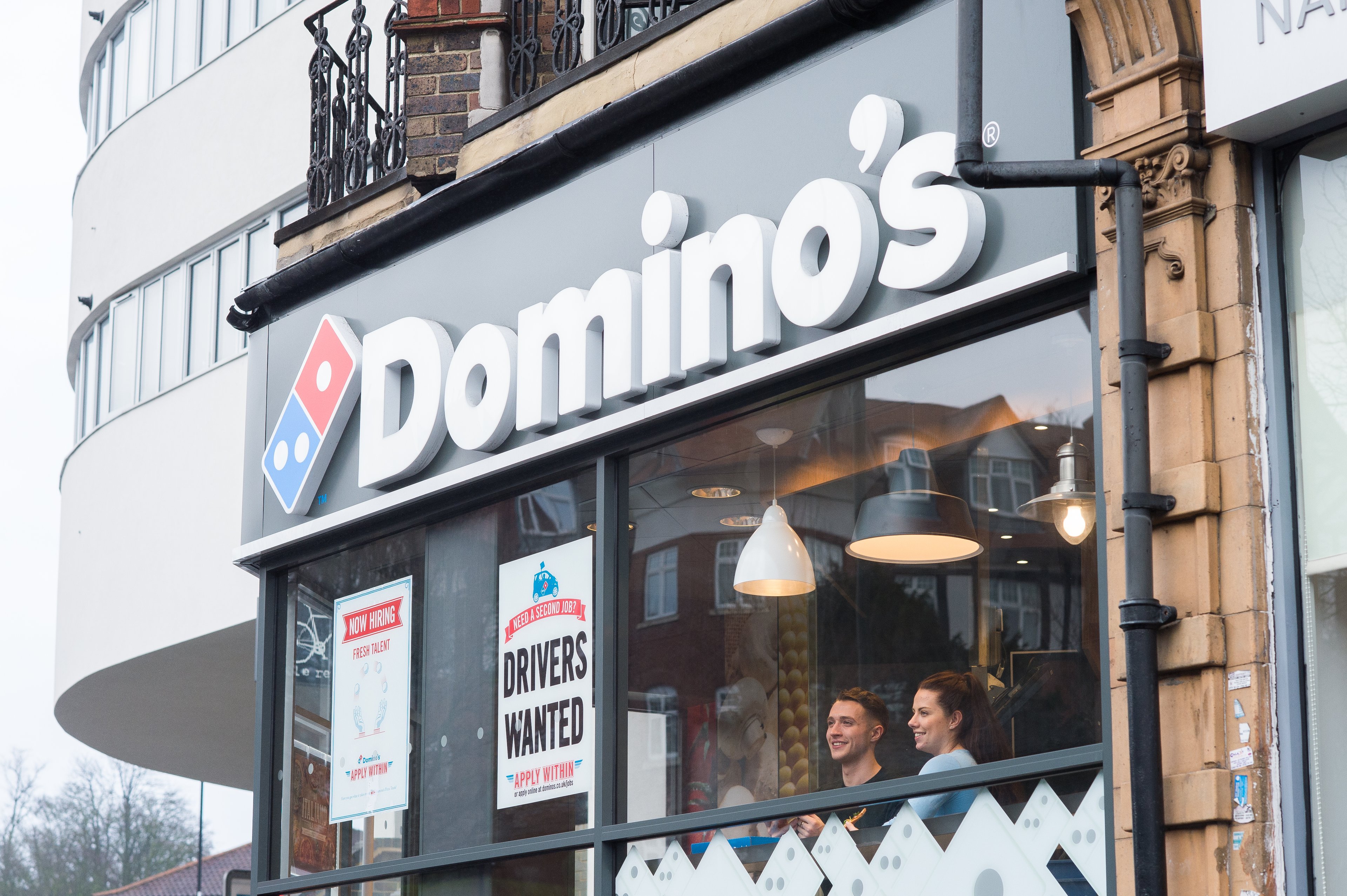 A Domino's storefront with two people looking out the street-facing window.