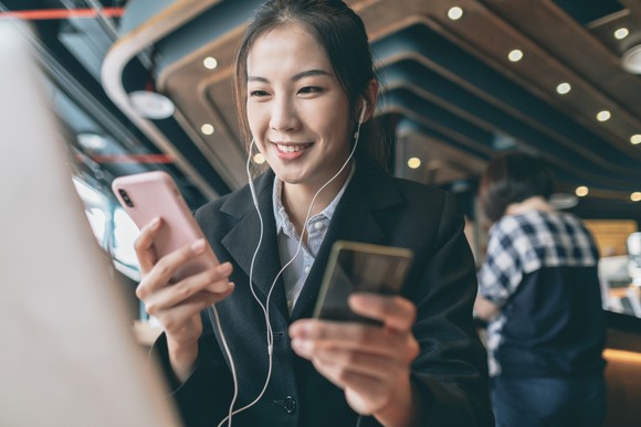 A young adult holding a smartphone and a credit card preparing to make a financial transaction.