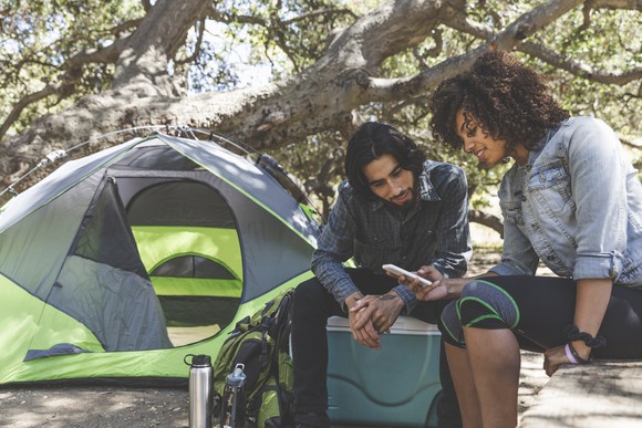 Two people sit outside of a pitched tent looking at a smartphone together