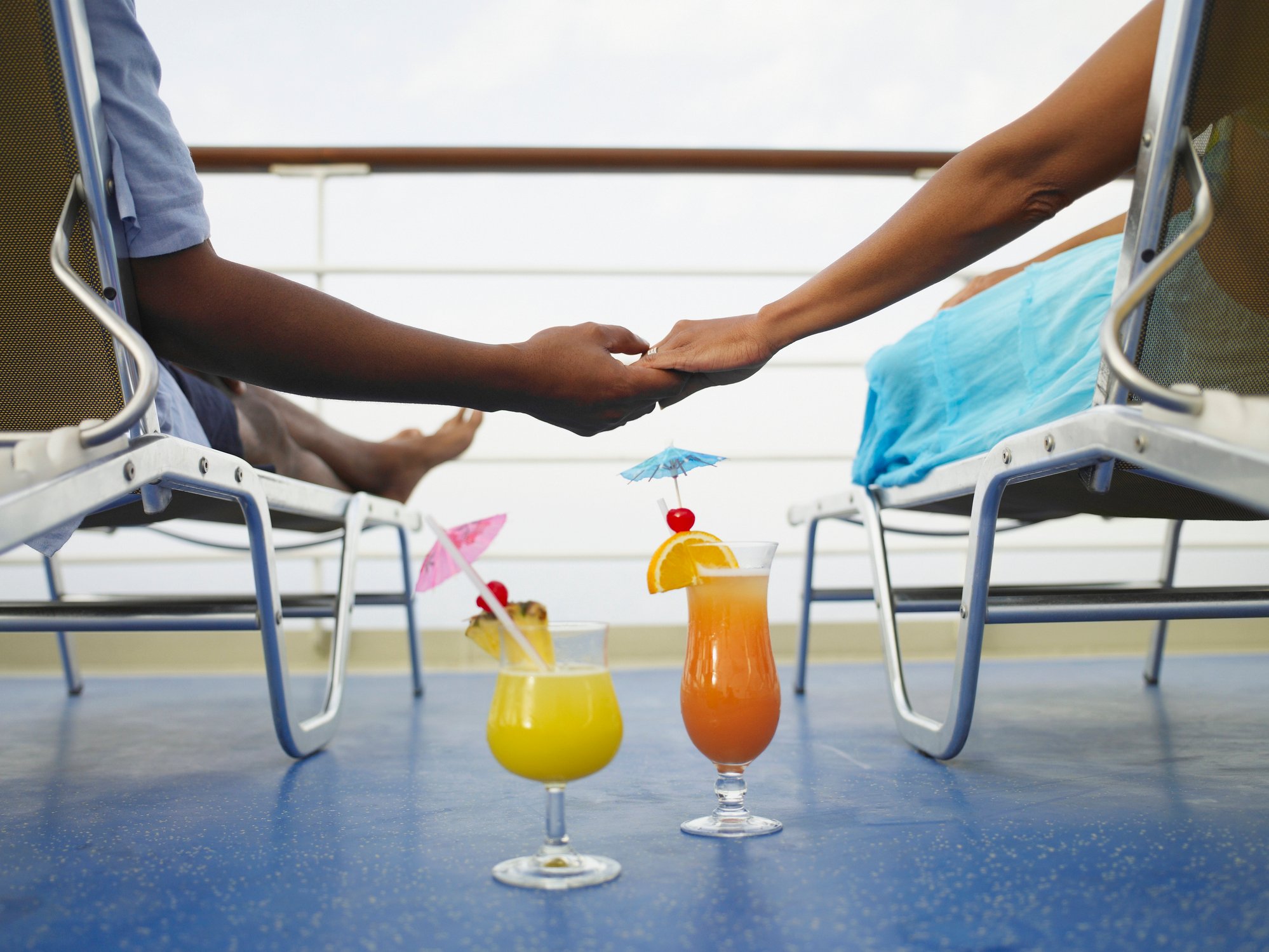 A couple holding hands on a cruise ship with umbrella drinks on the floor.