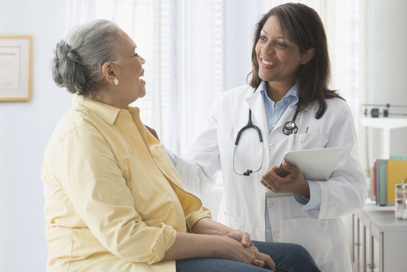 A smiling doctor meeting with an older patient who is sitting on the exam table.