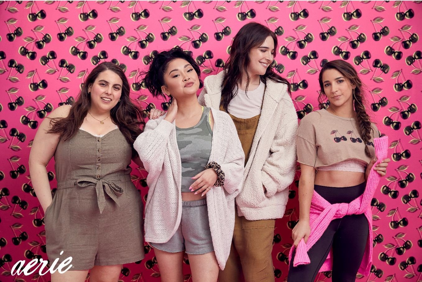 Four young women wearing loungewear pose in front of a pink background.