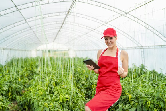 A greenhouse worker smiles while holding a tablet.