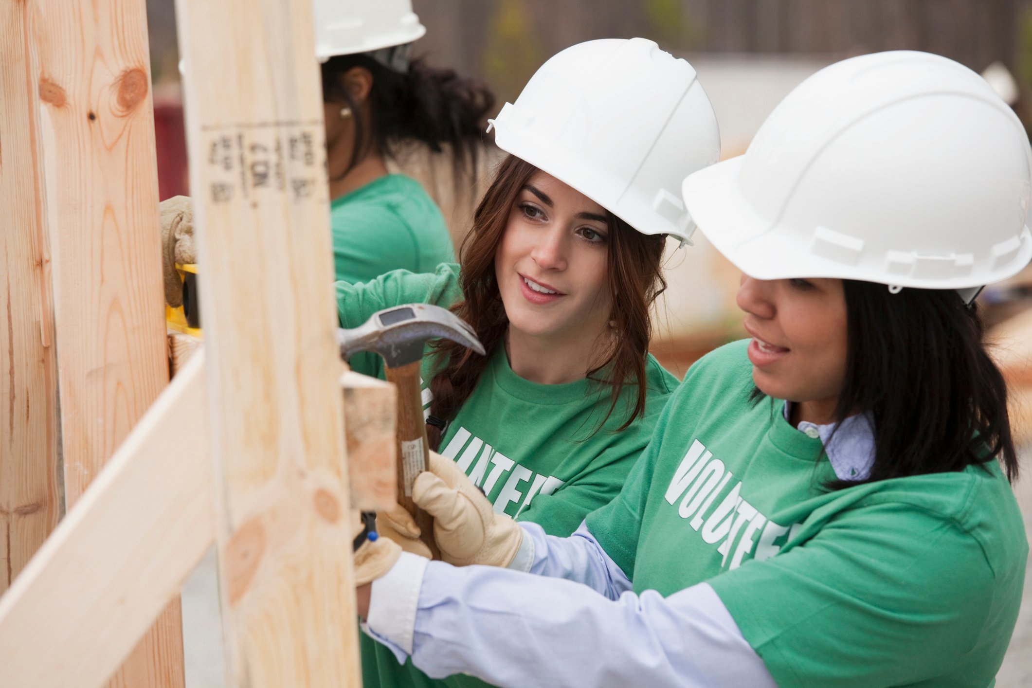 Three women in hard hats constructing a house at a job site. 