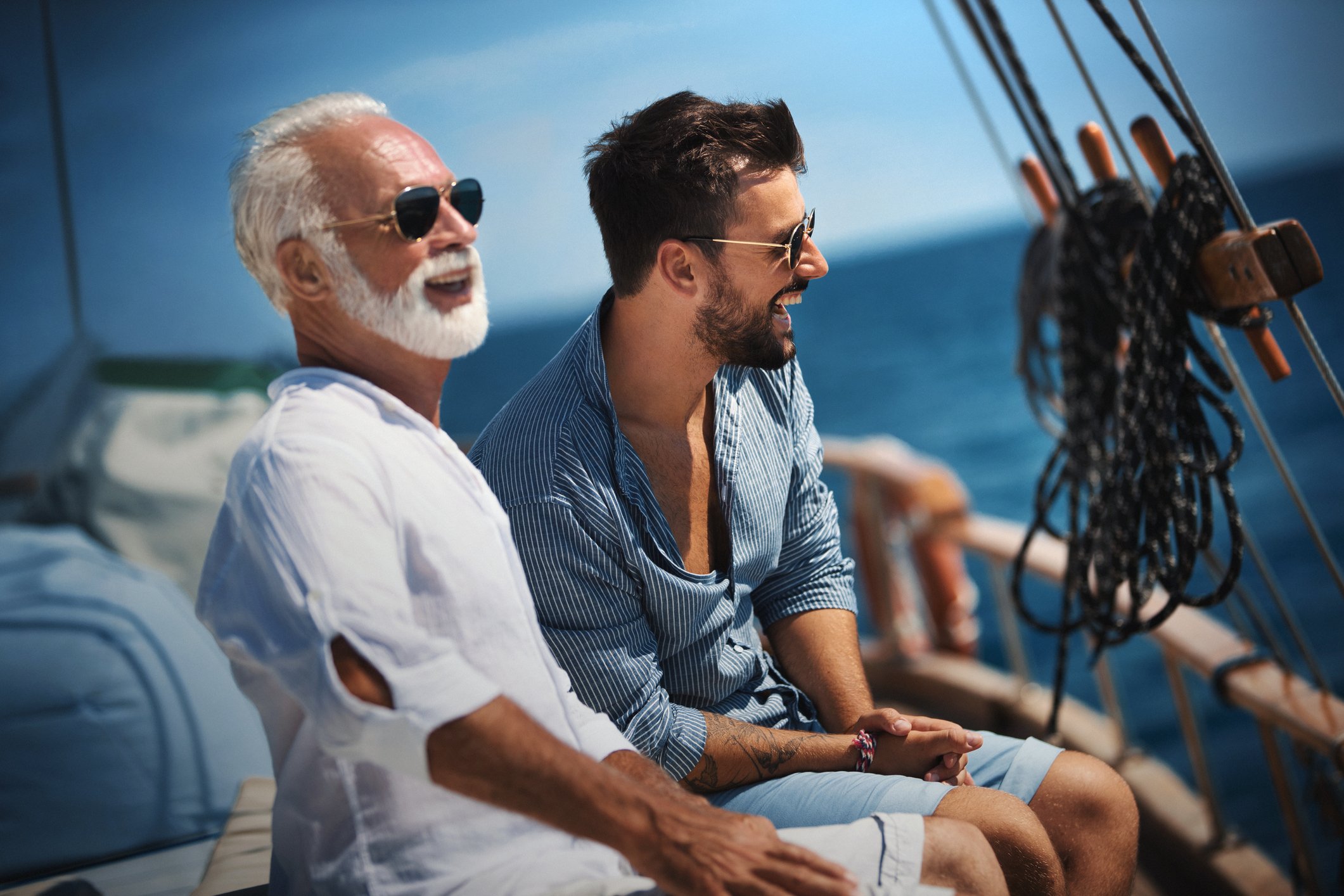 A couple wearing sunglasses enjoying themselves on a sailboat.