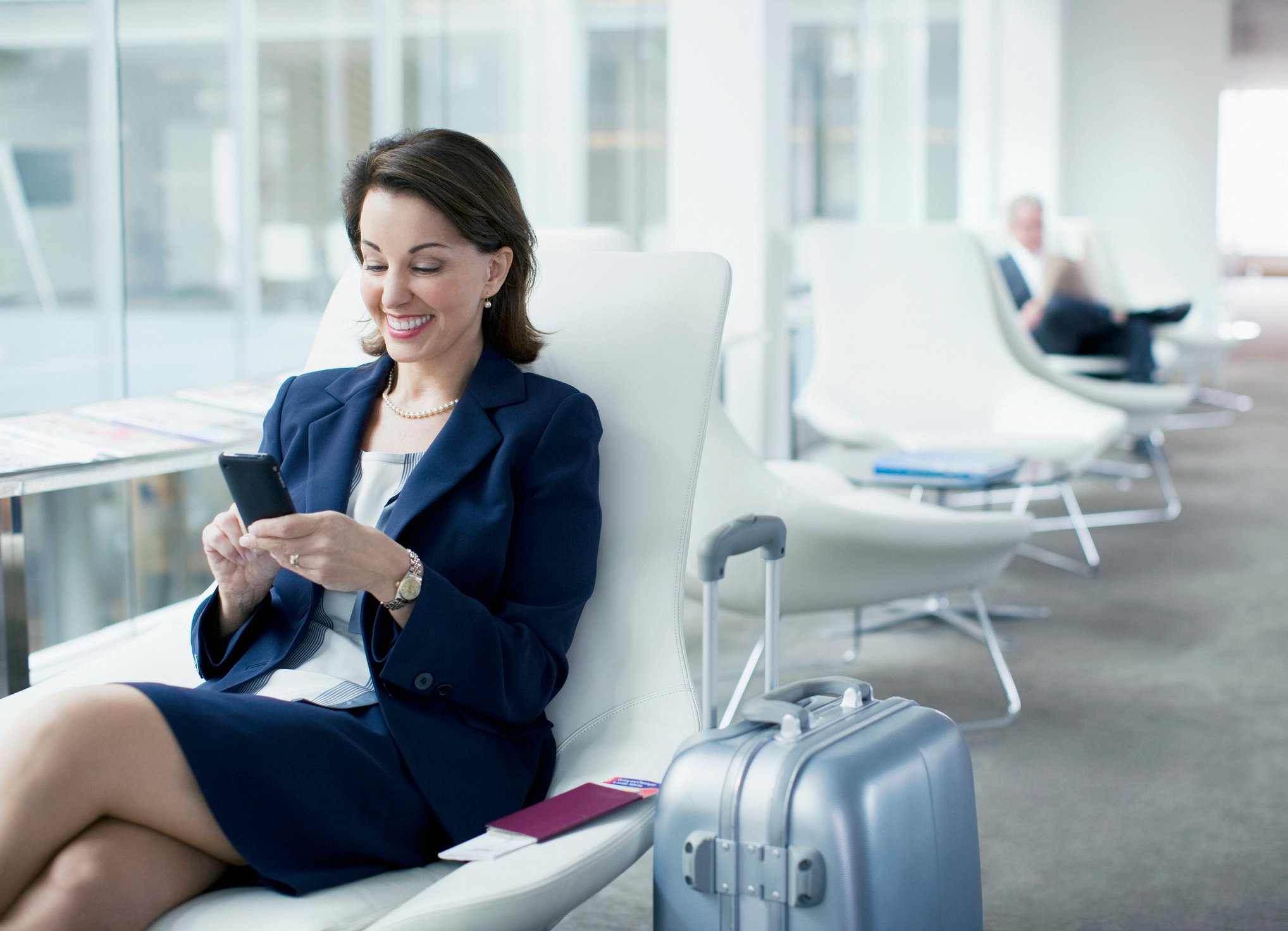 A woman waiting in an airport, looking at her phone, smiling. 