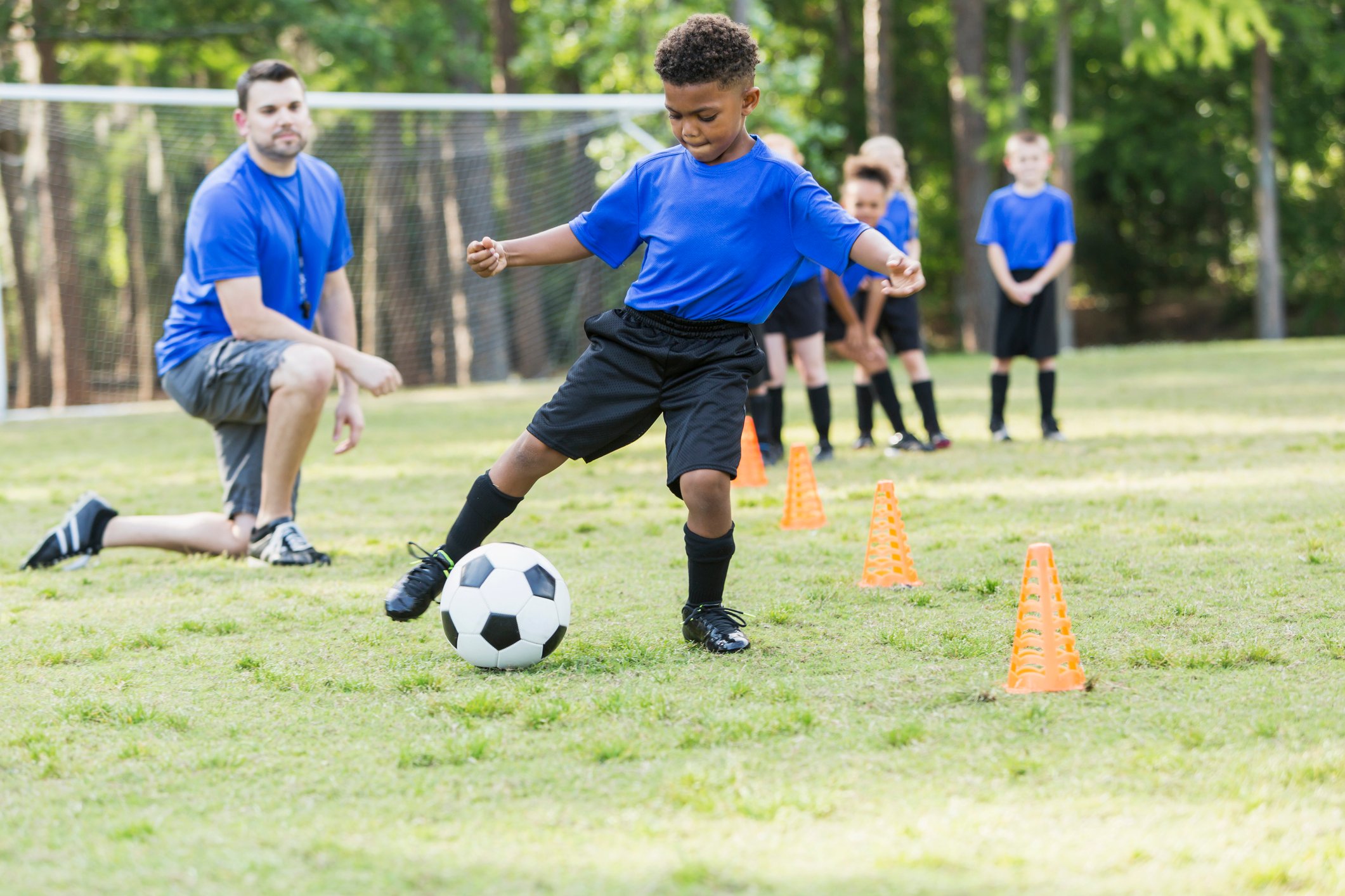 Youth soccer team with boy dribbling soccer ball while coach looks on.