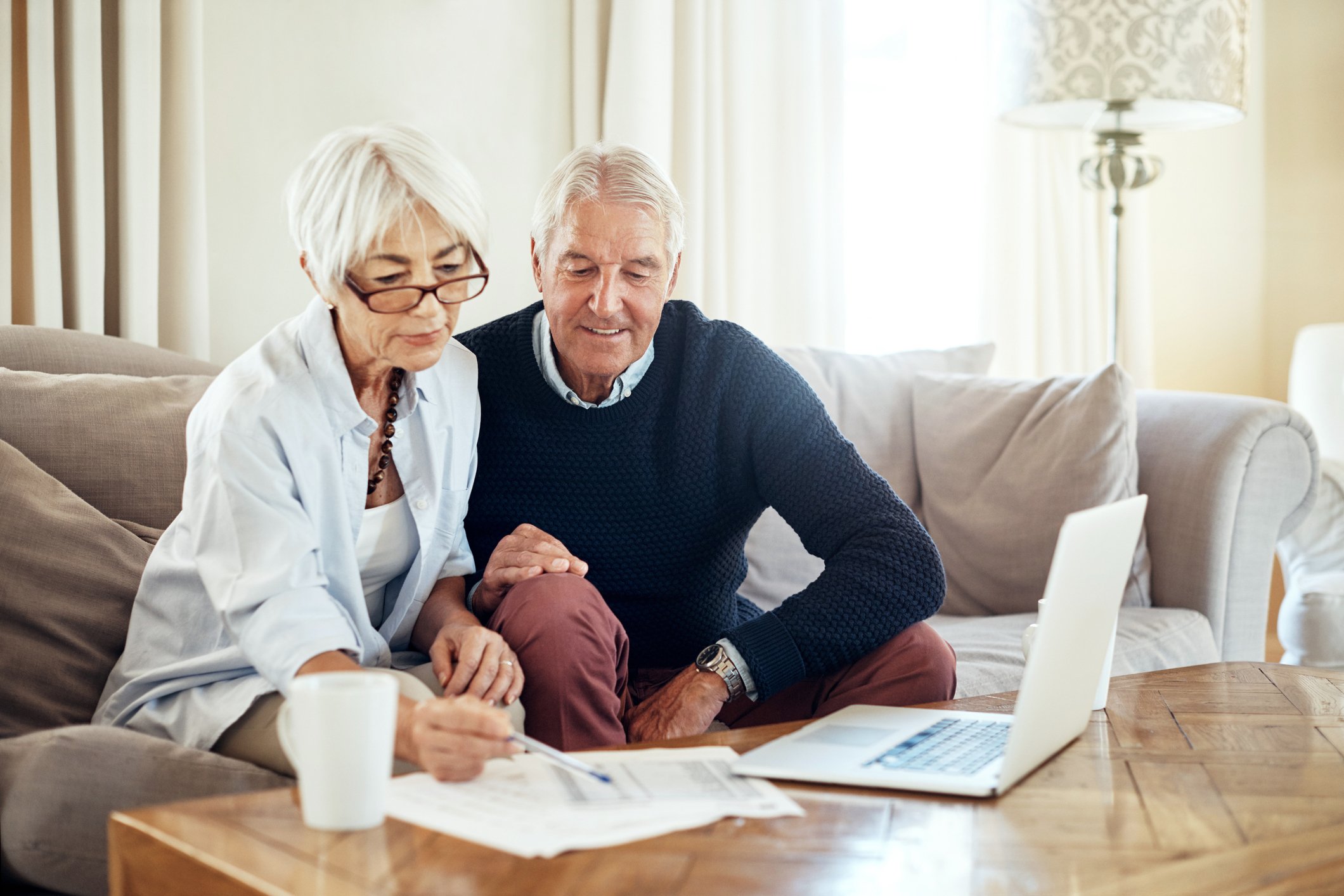 Two elderly people looking over finances in front of a computer sitting on a coffee table.