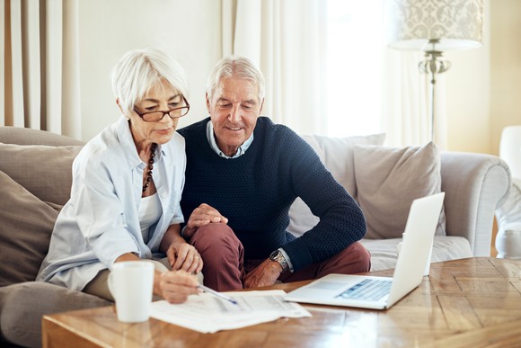 Two elderly people looking over finances in front of a computer sitting on a coffee table.