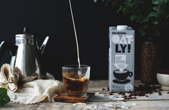 A box of Oatly next to coffee.