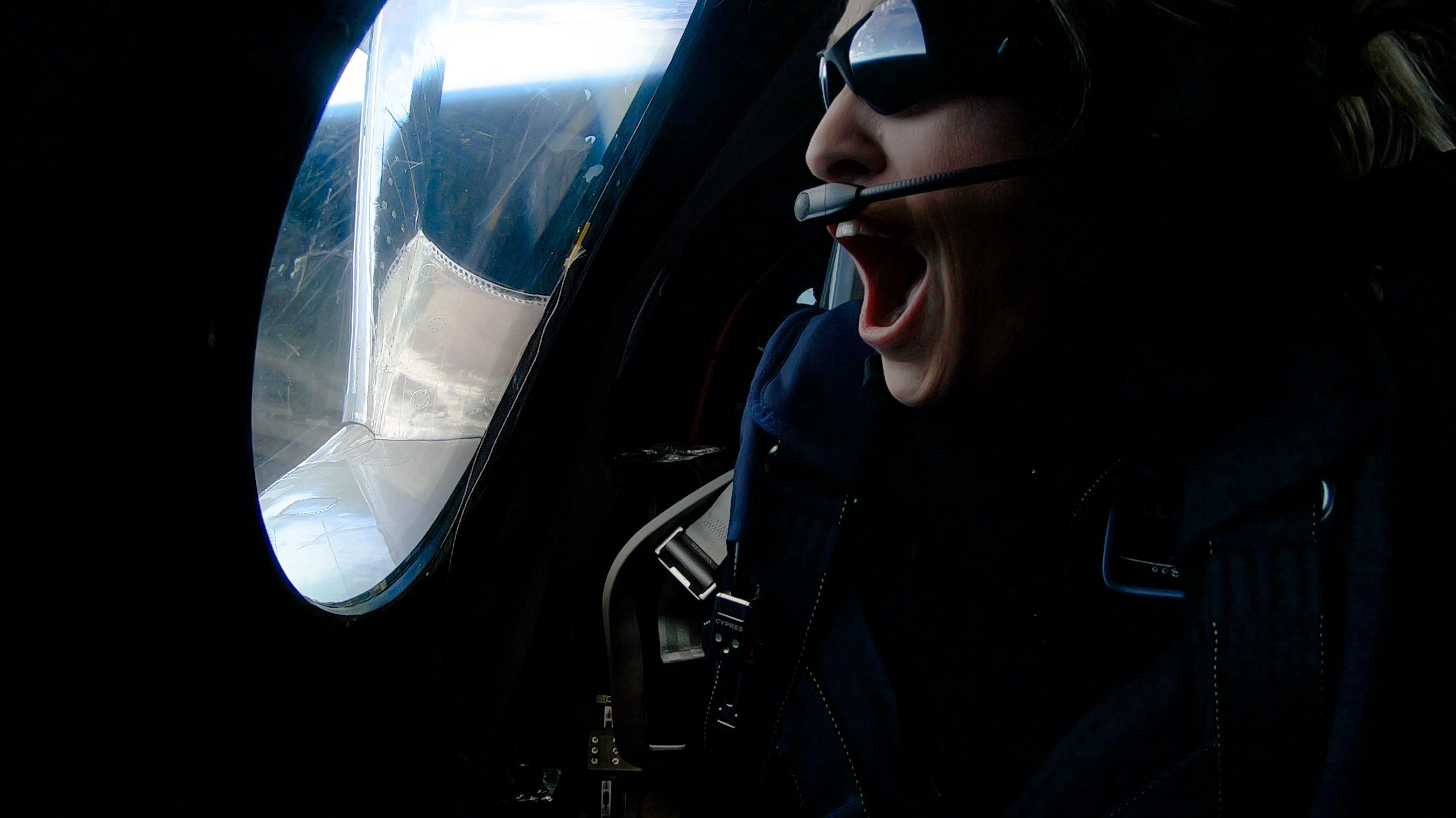 A person wearing a headset looks out the window of a space plane.