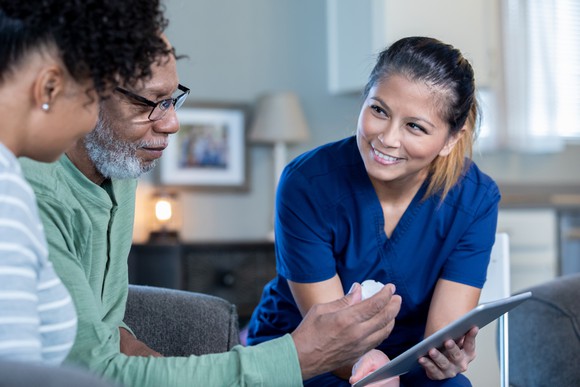 A nurse showing a seated couple something on an iPad she is holding.