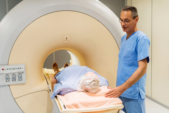 Doctor standing next to a male patient about to go through a medical imaging scan