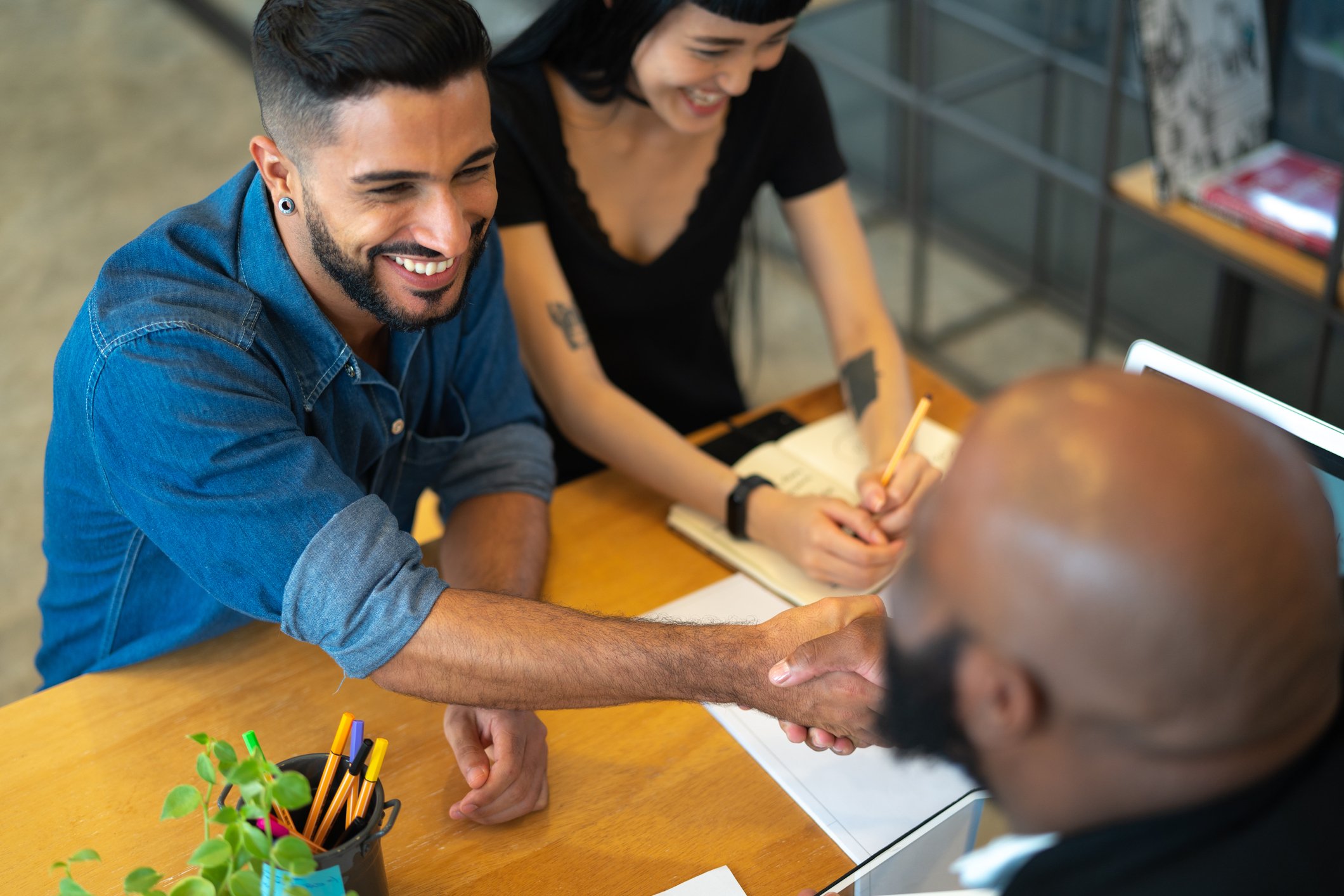 People shaking hands over table with paperwork.