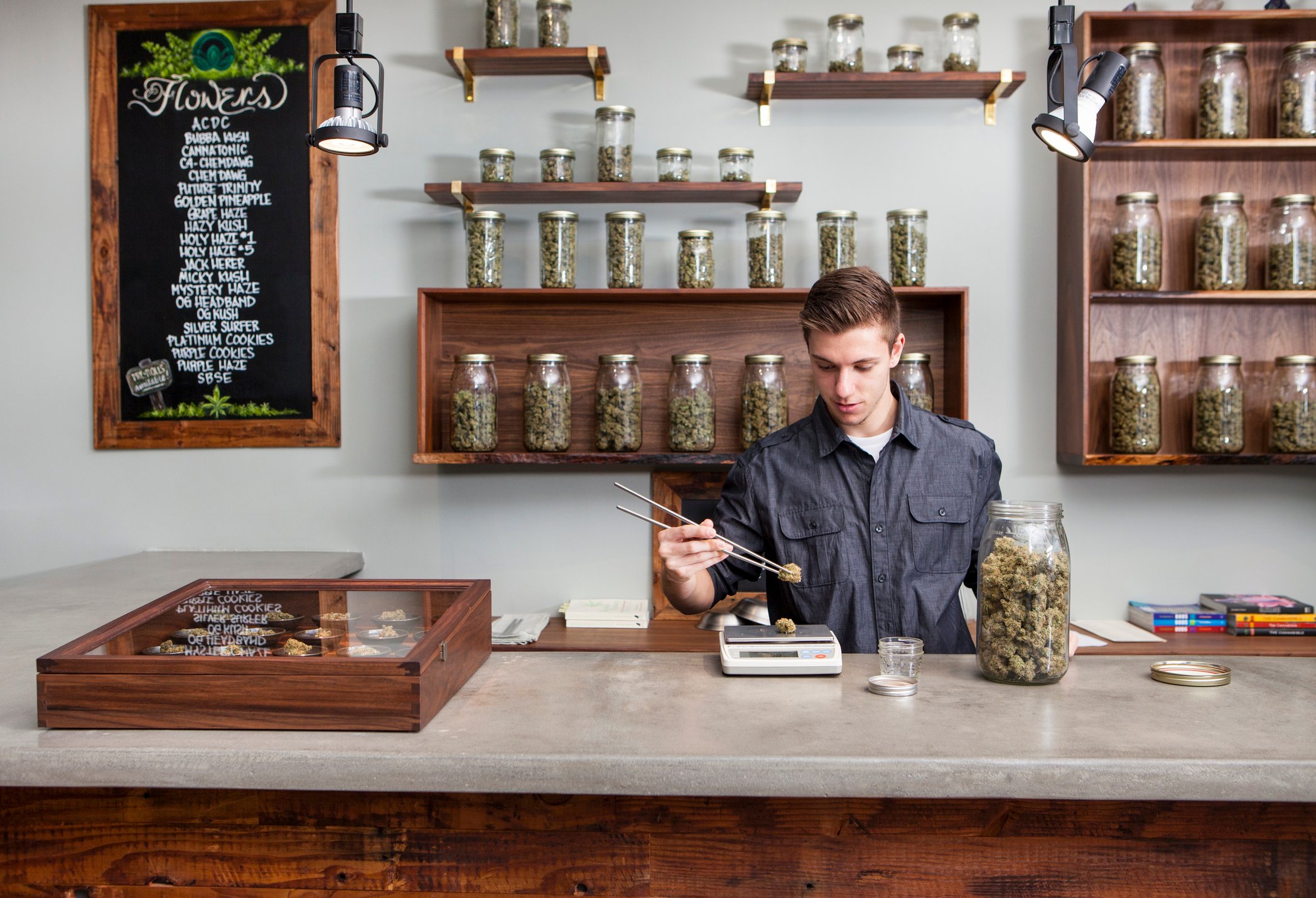 A worker weighs cannabis flower on a scale from behind the counter at a cannabis dispensary.