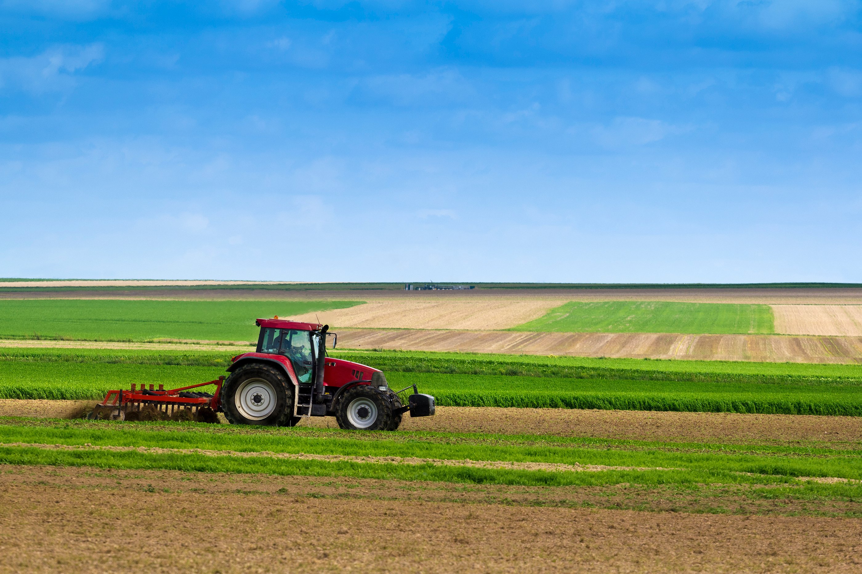 Red tractor farming in large field.