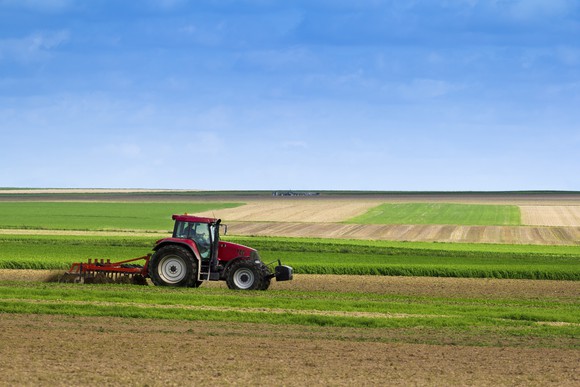 Red tractor farming in large field.