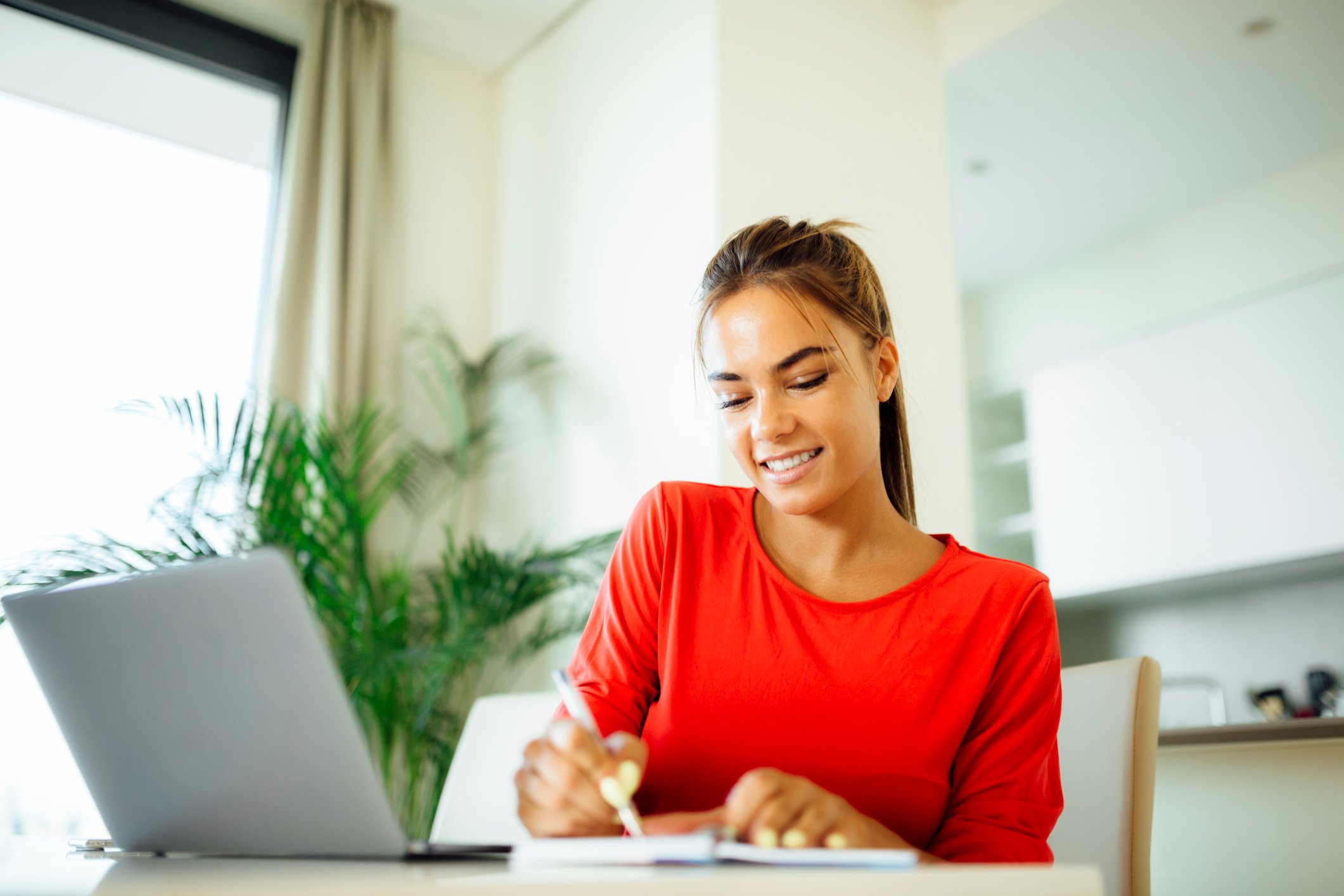 Woman sitting in front of a computer, crossing an item off a paper list.