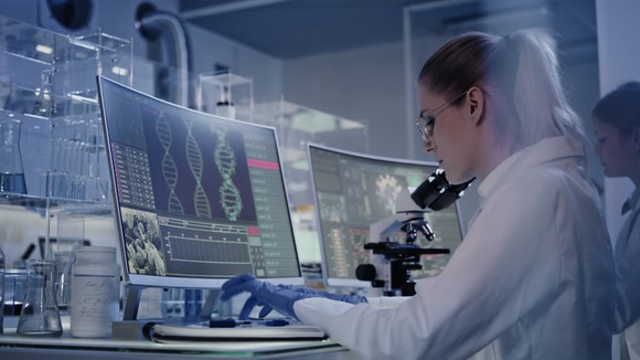 A researcher sitting at a computer screen with the DNA double-helix displayed.