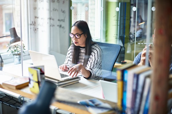 A woman using a laptop and sitting at a desk.