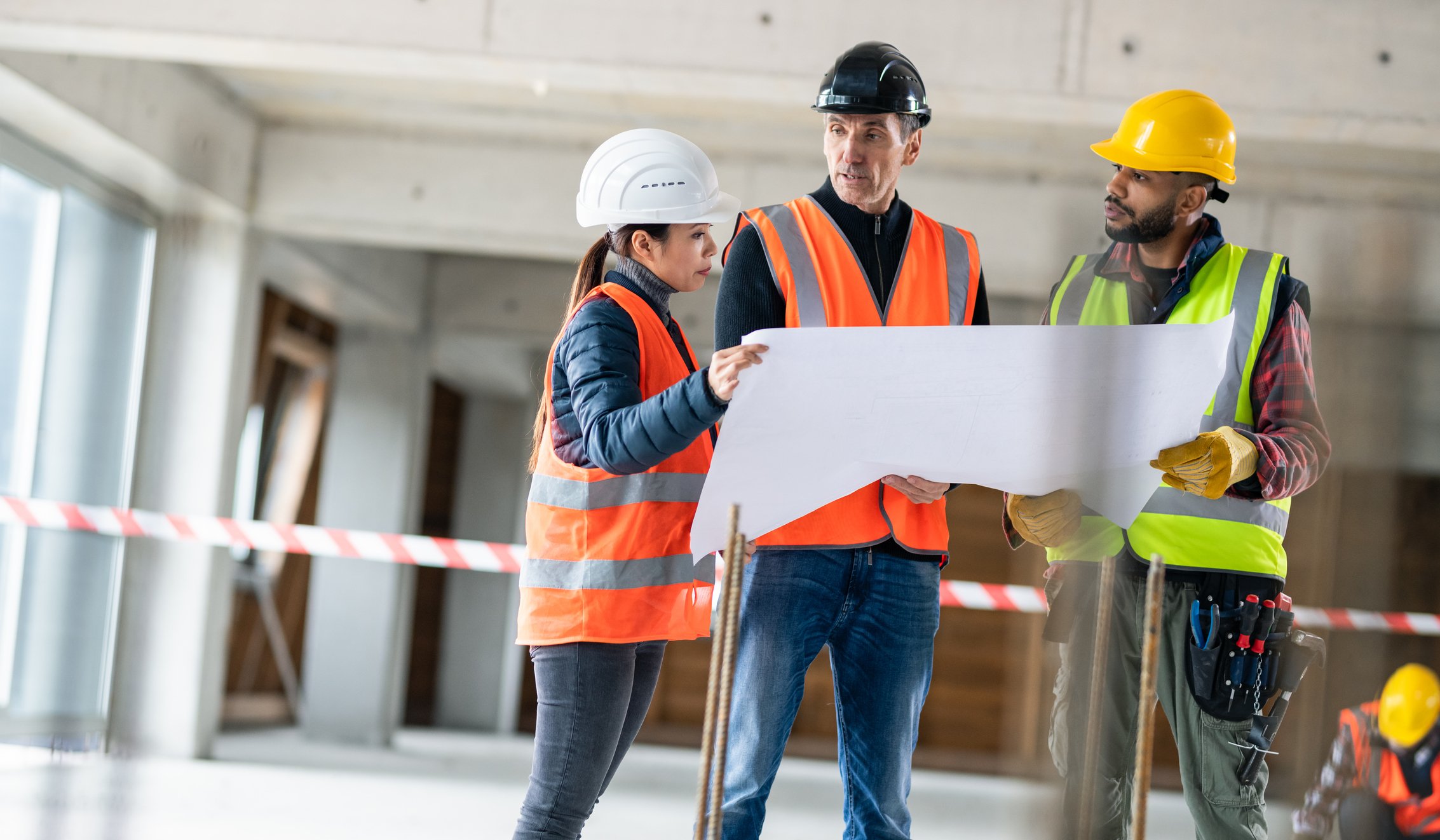 three workers in hard hats looking over a blueprint at a construction site
