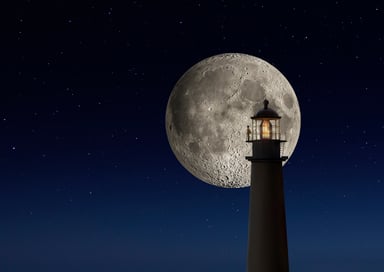 moon in the night sky behind a lighthouse