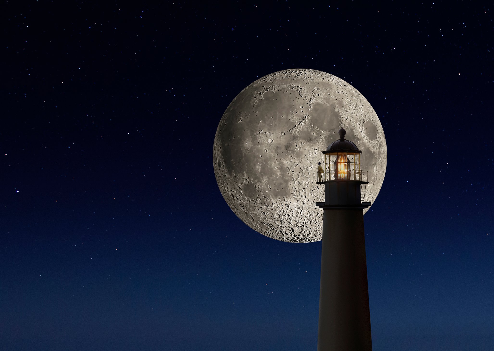 Moon in the night sky behind a lighthouse.