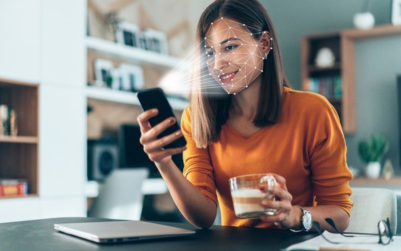 Young woman looks at smartphone in her home and the phone 3D senses her face. 