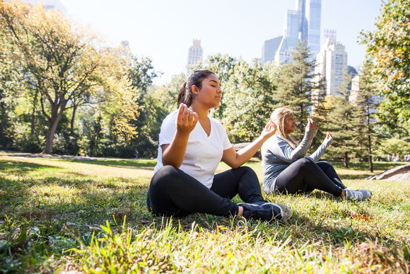 Two people in a yoga pose in a park lawn with skyline behind.