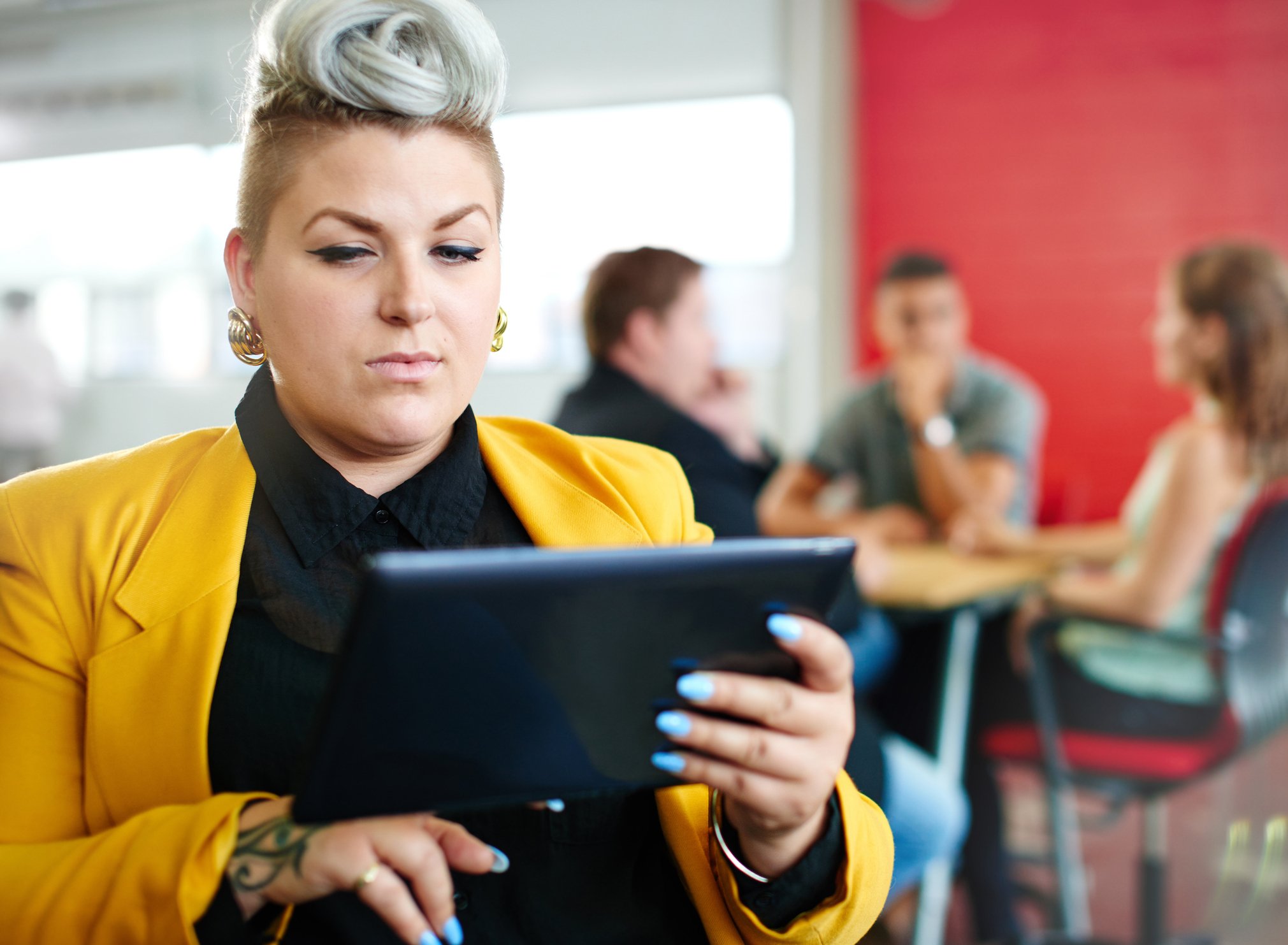A well-dressed person sitting indoors stares intently at their tablet device.