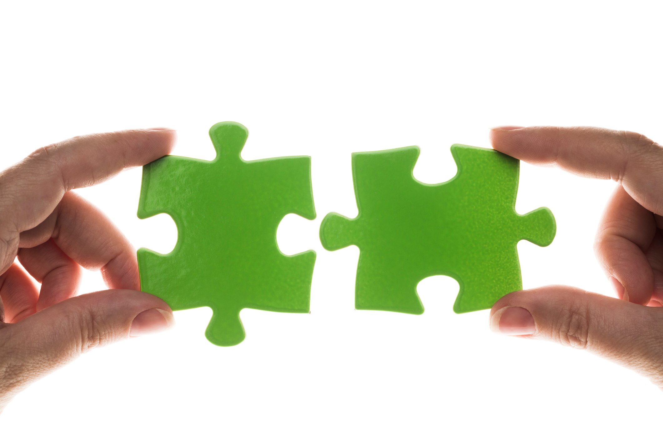 Hands holding two green jigsaw puzzle pieces close to each other.