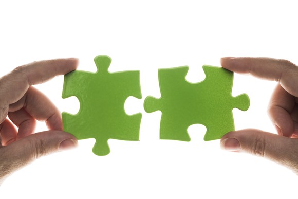 Hands holding two green jigsaw puzzle pieces close to each other.